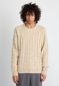 Bežni pleten jumper s kabelnim vzorcem, okroglega izreza in rebrastimi manšetami. Preraba vsebuje subtilne madeže barv za dodano teksturo.