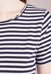 Randig t-shirt med marinblå och vita horisontella ränder, rund halsringning och mjukt bomullstyg med sömdetaljer.