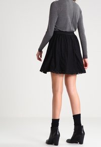 Jupe noire avec une finition texturée, coupe évasée et ourlet festonné, associée à un haut gris à manches longues et des bottines.