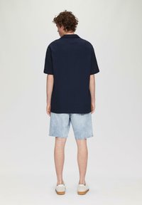 Marineblauw overhemd met korte mouwen en een kraag, gecombineerd met lichte denim shorts en witte sneakers. Glad materiaal en een ontspannen pasvorm.