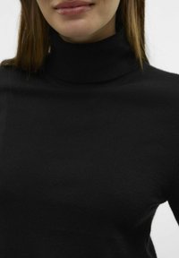 Črn pulover z visokim ovratnikom, izdelan iz mehkega, finega pletenega materiala. Ima oprijet dizajn z visokim ovratnikom in gladko teksturo. Minimalističen stil.