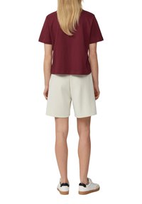 Bordeaux katoenen top met korte mouwen, gecombineerd met witte shorts. Sneakers hebben een witte body en een zwarte hakaccent. Glad textuur en een relaxte pasvorm.