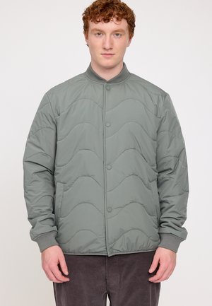 Hellgraue gepolsterte Jacke mit gewelltem Steppmuster, Druckknöpfen und gerippten Bündchen. Sie verfügt über zwei Seitentaschen und einen Stehkragen.