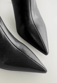 Svarta högklackade stövlar med en strukturerad, reptilmönstrad läderfinish. Spetsiga tår och smal silhuett.