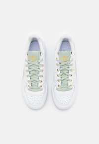 Sneakers bianche con accenti verde chiaro e occhielli dorati. Punta forata, lacci piatti e logo sulla linguetta e sul lato. Design atletico standard.