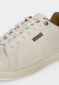 Λευκό χαμηλό sneaker με λευκά κορδόνια, καφέ εσωτερική επένδυση και λογότυπο Jack & Jones στο πλάι και κοντά στον γιακά.