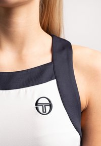 Ärmelloses Oberteil mit schwarz-weißem Design; glattes Material; mit einem runden, in Schwarz auf dem weißen Bereich gestickten Logo.