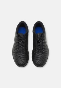 Un par de zapatillas deportivas negras con superficies texturizadas, cordones negros, plantillas azules y un logo blanco en los laterales, vistas desde arriba.