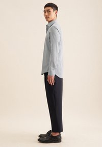 Camicia button-up a quadri blu chiaro, pantaloni scuri e scarpe nere. La camicia presenta un colletto e maniche lunghe; silhouette pulita e strutturata.