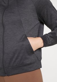 Mörkgrå zip-up jacka med en texturerad tyg, åtsittande ärmar, sidofickor och en nederkant som sitter vid midjan.