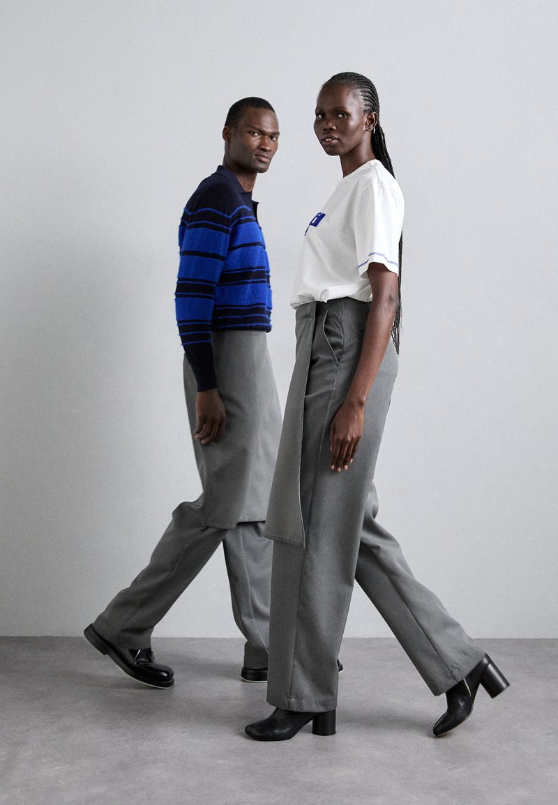 Maglione blu a righe e t-shirt bianca con dettagli blu, abbinati a pantaloni grigi a gamba larga e stivali neri con tacco quadrato.