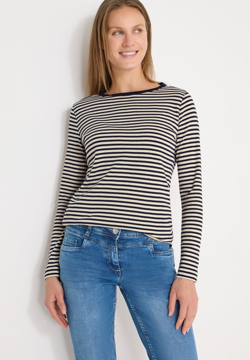 Haut à manches longues avec rayures horizontales bleu marine et crème, encolure ronde, et texture de tissu douce, assorti à un jean en denim bleu.