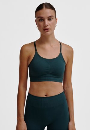 Dunkelgrüner Sport-BH mit dünnen Trägern, rundem Ausschnitt und gerippter Textur. Der Stoff ist glatt mit subtilen Raffungen an der Vorderseite.