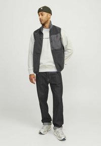 Herenoutfit met een grijze fleece vest met een ritszak, grijze sweatshirt, donkerblauwe jeans en zilveren sneakers met lichte accenten.
