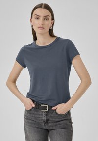 Dunkelblaues kurzärmliges T-Shirt aus weichem Stoff, mit Rundhalsausschnitt und glatter Textur, getragen zu schwarzen hoch geschnittenen Jeans.