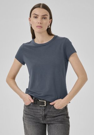 Dunkelblaues kurzärmliges T-Shirt aus weichem Stoff, mit Rundhalsausschnitt und glatter Textur, getragen zu schwarzen hoch geschnittenen Jeans.