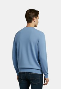 Maglione blu girocollo con maglia testurizzata, maniche lunghe e polsini a costine. Abbinato a jeans in denim scuro, presenta un design semplice e casual.