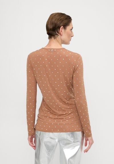 Cămașă lungă maro cu mânecă lungă și guler rotund, având embellishment-uri argintii într-un model dispersat, asortată cu pantaloni argintii strălucitori.