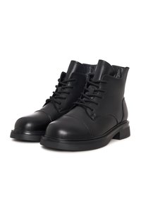 Botas de cuero negras hasta el tobillo con cordones en la parte frontal, puntera redondeada y tacones bajos en un fondo blanco.