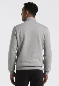 Grauer Pullover mit hohem Kragen, aus einem weichen Material gefertigt. Verfügt über taillierte Bündchen und einen Taillenbund und besticht durch ein schlichtes, elegantes Design.