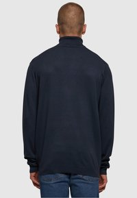 Mørkeblå genser med høy krage, lange ermer og ribbede mansjetter. Glatt tekstur, ledig passform og minimalistisk design, uten synlige logoer.
