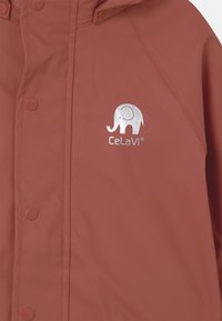 Nepremokavá detská pršiplášť v hrdzavej farbe, vyrobený z hladkého materiálu so strieborným logom slona a patentkami vpredu.