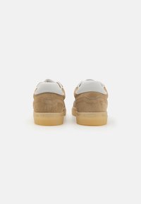 Brune suedef sneakers med hvite skinnaccentuer, rund form, gummisåle og minimalistisk sømdetalj på baksiden.