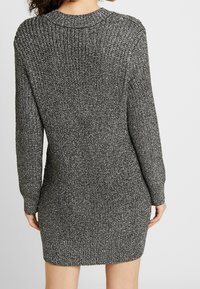 Robe en maille aux textures noire et argentée, silhouette ajustée, manches longues, col et ourlet côtelés. Vue arrière détaillée mettant en valeur le matériau.