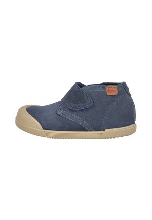 Zapato de ante azul marino con cierre de velcro, suela de goma beige, puntera redondeada y detalle de costuras contrastantes. Diseño de tacón redondeado.