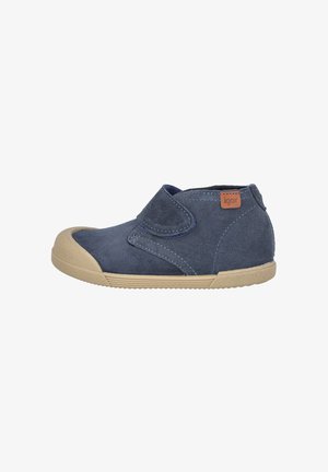 Zapato de ante azul marino con cierre de velcro, suela de goma beige, puntera redondeada y detalle de costuras contrastantes. Diseño de tacón redondeado.