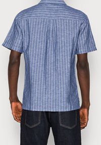 Korte mouwen overhemd in blauwe chambray stof met witte verticale strepen; heeft een standaard kraag en een rugpasdetail.