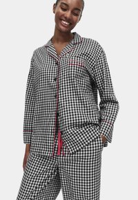 Sort-hvid ternet pyjamassæt med rød piping. Langærmet top med knaplukning og lomme; matchende bukser med snøre.