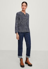 Blusa a righe blu scuro con scollatura bottonata, abbinata a jeans blu scuro arrotolati e stivaletti marroni con suola spessa.