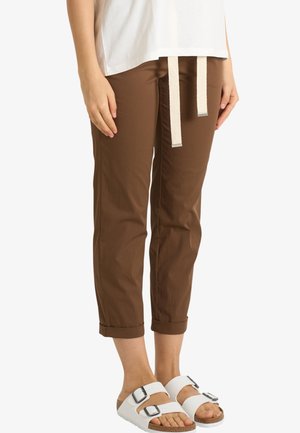 Persona che indossa pantaloni marroni corti con coulisse beige, una camicia bianca e sandali bianchi con doppi fibbie.