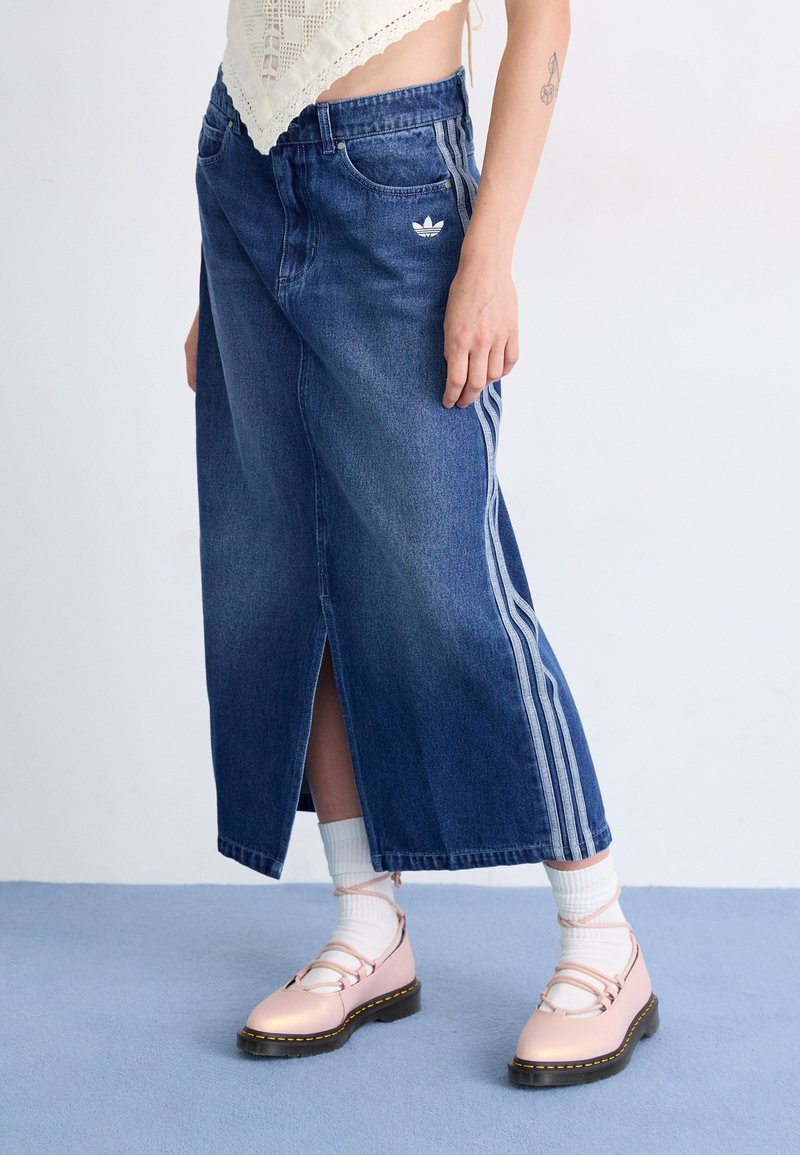 Farmernadrág maxi szoknya, kék oldalsó hasítékkal, fehér Adidas logóval és háromcsíkkal mindkét oldalon. Világos rózsaszín cipővel párosítva.