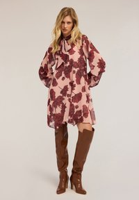 Floral Shift-Kleid aus pinkem Chiffon mit kastanienbraunen Blattformen, mit einem Bindekragen und langen Ärmeln. Kombiniert mit braunen Overknee-Stiefeln.