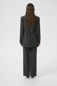 Grijze op maat gemaakte pak met een lange blazer en brede broekspijpen. De stof lijkt glad met een subtiele textuur. Achteraanzicht toont een ontspannen pasvorm.