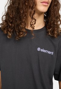Schwarzes Baumwoll-T-Shirt mit kurzen Ärmeln, das ein dezentes lila "Element"-Logo auf der linken Brustseite zeigt. Reguläre Passform, glatte Textur.
