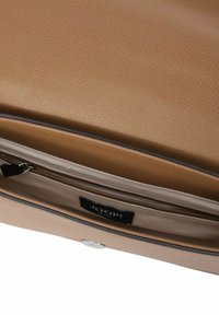 Wnętrze brązowej skórzanej torby o teksturowanej powierzchni z kieszenią na zamek błyskawiczny oraz metką z logo. Smukły fason z jasnym wykończeniem i metalowymi elementami.