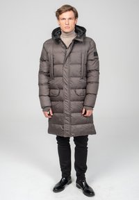 Donkergrijze pufferjas met horizontale stiksels, zijzakken en een capuchon, gecombineerd met zwarte slim-fit broek englanzende zwarte schoenen.