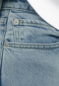 Blugi din denim de culoare bleu deschis, cu o textură estompată, având cusături galbene în contrast și două nasturi din metal argintiu pe buzunarul din spate.