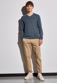 Pull en V en tricot bleu foncé, associé à un chino beige et des baskets claires. Design simple sans motifs ni accents supplémentaires.