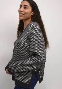 Adīts džemperis ar tumši zilu un krēmkrāsas rakstu, ar garām piedurknēm un sānu atvērumiem. Audums šķiet teksturēts un silts.