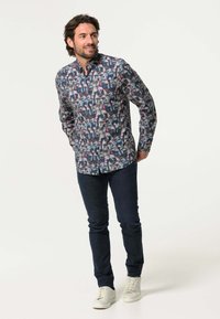 Overhemd met knoopsluiting met een multicolore vogelprint op een donkere achtergrond, gecombineerd met donkere jeans en witte sneakers. Vrije pasvorm, lange mouwen.