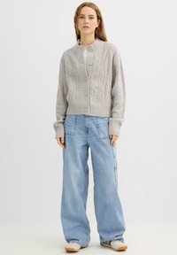 Cárdigan gris de punto con cuello redondo, cierre de botones y puños acanalados, combinado con pantalones cargo holgados de mezclilla azul claro.