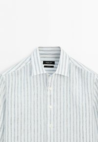 Chemise blanche boutonnée avec fines rayures verticales bleues et col pointu, posée à plat sur un fond blanc uni.