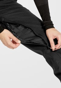 Zwarte sportbroek met een ritssluiting, voorzien van een textuur aan de binnenkant. Het materiaal is soepel met een aansluitend ontwerp en minimale branding.