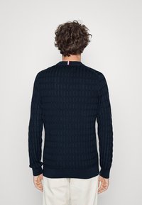 Donkerblauwe textuursweater met een geribbeld breipatroon, ronde hals en contrasterende rode en witte accenten bij de kraag.