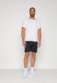 Camiseta deportiva de manga corta blanca y pantalones cortos negros, usados con zapatillas blancas. La camiseta presenta un logo en el pecho. Materiales suaves y ligeros.