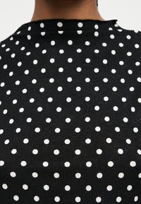 Πλάτη ενός ατόμου που φορά ένα μαύρο ύφασμα με λευκές πουά, ομοιόμορφα κατανεμημένες, και ελαφρώς ραμμένη στρογγυλή λαιμόκοψη.